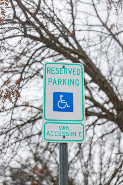 Close-up view of a rectangular traffic sign attached to a metal pole in a residential street. The sign features a black silhouette of a shoe with chewing gum stuck underneath, crossed out with a red circle and diagonal line. Below the symbol, there is a red rectangular box with white text that reads, 'Don't drop gum.' In the background, there are vehicles parked along the curb, including a white car and a red car, with a row of brick houses and trees with green foliage across the street. The scene is illuminated by bright daylight, highlighting the clean pavement and well-kept houses, and the image relates to urban signage that may be relevant in contexts like house removals or local regulations overseen by Hounslow Council, as referenced in the page about rules for skip permits and removal vans, provided by Hounslow Man and Van.